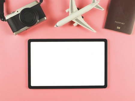 Top view or flat lay of digital tablet with blank white screen, airplane model, passport and digital camera isolated on pink background. travel planning concept.の写真素材