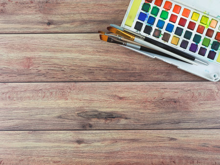 Top view or flat lay of artist workspace. Drawing tools, stationary supplies, Watercolor paints and brushes on wooden table, copy space.の写真素材