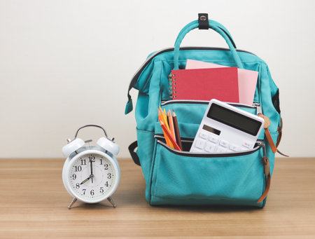 Back to school concept.Front view  of green backpack with school supplie and white vintage alarm clock 8 o'clock on wooden table and white  background with copy space.の写真素材