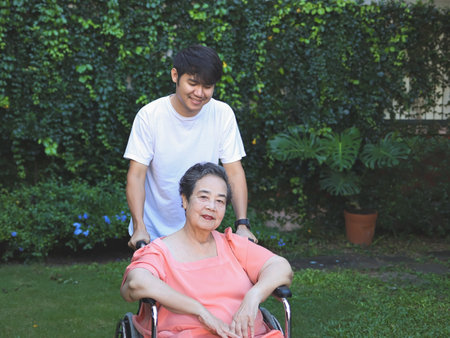 Portrait of Asian senior woman sitting on wheelchair with her son in the garden.の写真素材