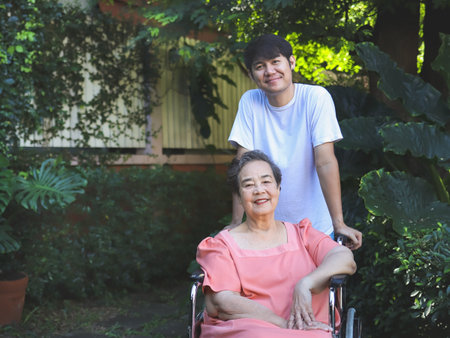 Portrait of Asian senior woman sitting on wheelchair with her son in the garden.の写真素材