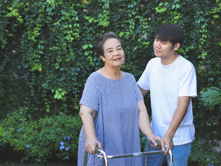 Portrait of Asian elderly woman walking in the park with orthopedic walker ,helping of her son. Physical activity of old age concept.の写真素材