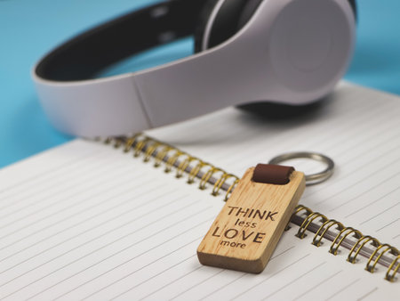 Close up image of wooden keyring with word "Think less love more" on diary with headphone on blue background.の写真素材