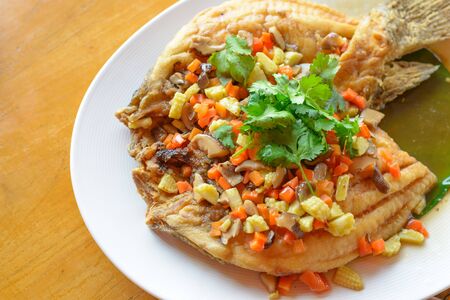 Deep fried fish with stir fried vegetables on white dish.