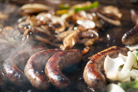 Grilled brats, green peppers and onions on the grill of a food truck surrounded by smoke with focus on center brats.の写真素材