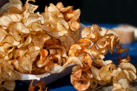 Freshly made hot curly potato chips overflowing onto  blue tablecloth.の写真素材
