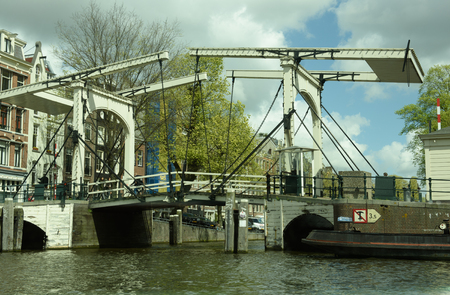 Ancient Draw Bridge over a canal with barge vessel nearby in the city of  Amsterdam in Netherlands.の写真素材