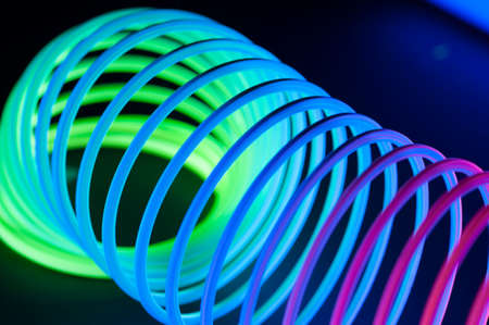Multi-colored circular spiral objects are viewed in close and lit with fluorescent colors against a deep blue background.の写真素材