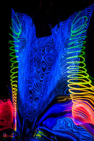 Fuzzy and circular objects in a close-up view and reflections are lit with fluorescent colors against a deep blue background.の写真素材