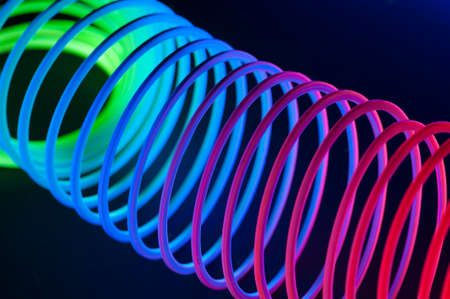 Multi-colored circular spiral objects are viewed in close and lit with fluorescent colors against a deep blue background.の写真素材