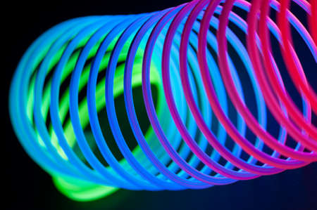Multi-colored circular spiral objects are viewed in close and lit with fluorescent colors against a deep blue background.の写真素材