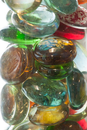 Multicolored glass orbs are viewed close-up and grouped together in a glass jar against a white background.の写真素材