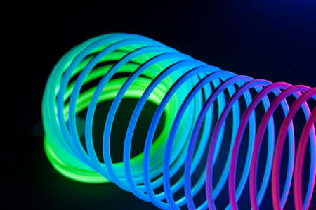 Multi-colored circular spiral objects are viewed in close and lit with fluorescent colors against a deep blue background.の写真素材