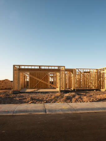 Wooden frame of a single house on a dirt lot showing only the timber walls before siding and roof in early morning light in a vertical view of the lot.のeditorial素材