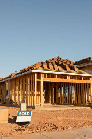 A new house construction with the wood frame before the siding stands next to an empty dirt lot with a sold sign, horizontal view.のeditorial素材