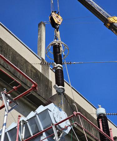 A close-up of a worker using a crane to install a large, ceramic electrical insulator on a...