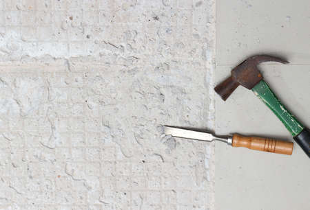 A hammer for hammering nails and a wood chisel is placed beside the area being newly tiled.