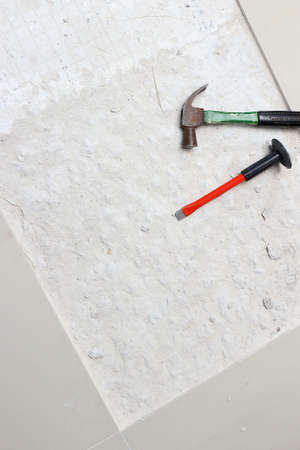 A hammer and a chisel hammer for drilling concrete is placed beside the area being newly tiled.