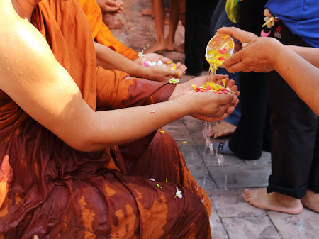During the Songkran festival, long lines form as devotees patiently await their turn to perform a traditional water-pouring ceremony for Buddhist monks. Using small bowls, they gently pour fragrant floral-infused water onto the monks' palms as a mark of respect.の写真素材