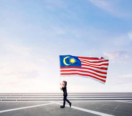Happy boy running while holding Malaysia flag on open space. Happy National Day.の写真素材