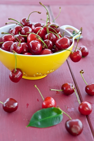 Fresh cherries in a yellow sieve on a dark red wooden backgroundの写真素材