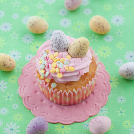 Little cupcake with frosting and colorful easter eggs on green