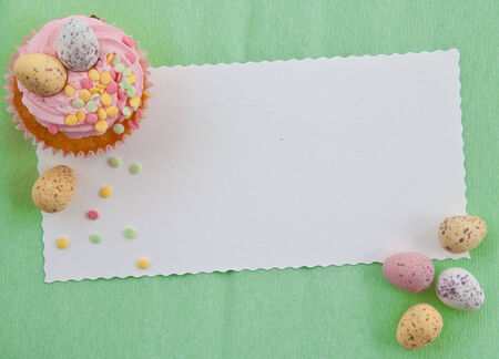 Little cupcake with frosting and colorful easter eggs on pinkの写真素材