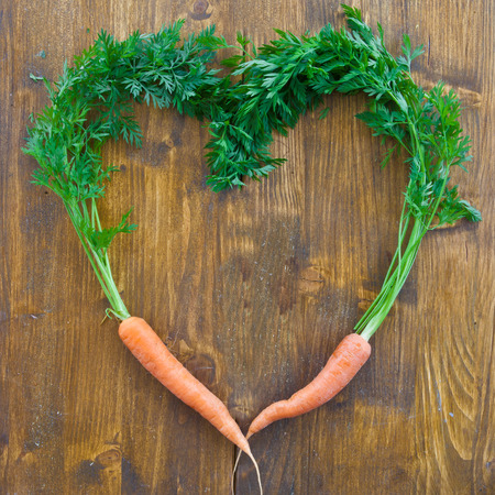 Fresh carrots with green leaves in a heart-shape on woodの写真素材