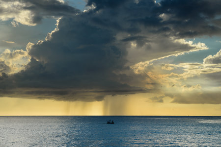 Small boat sailing in a calm sea and with the storm and clouds approaching on the horizonの写真素材
