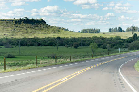 A lonely road and some hills on the background in Uruguay, next to TacuarembÃ³. The sky is full of small clouds and some trees on the rightの写真素材
