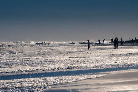 Sunset on the beach with some children playing on the shore. Some surfers entering the water and some fishermen in the background of the imageの写真素材