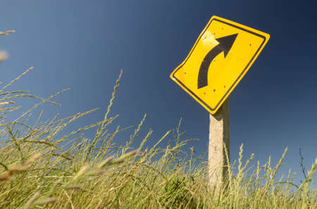 Right turn sign. Traffic sign depicting a right turn on the road. Deep blue background. An area with grass can be seen on the bottom. Road towards San Ramon, Canelones, Uruguayの写真素材