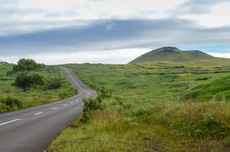 Zigzagging road in the countryside of Easter Island, with some volcanic formations on the horizonの写真素材