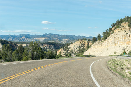 Lonely road between mountain ridges with some trees on each side of the road that turns to the right, somewhere in Utah, United Statesの写真素材