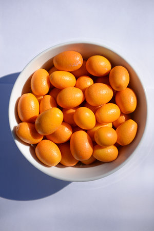 White bowl filled with small kumquats, in the sunの写真素材
