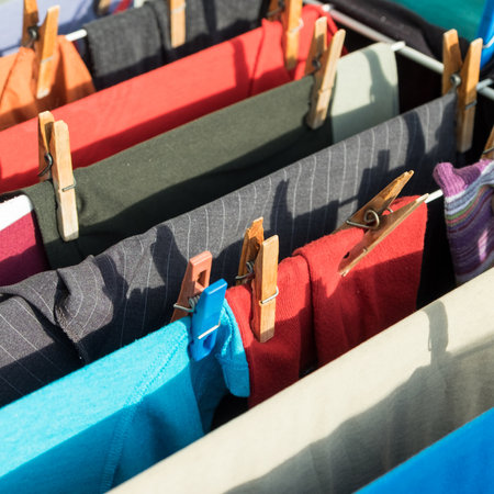 Clothes hanging on a clothesline, with a blue shirt hanging in the middle. The clothes are all...
