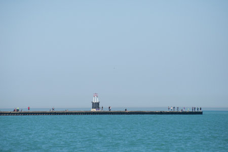 A pier with a lighthouse and a group of people standing on it. The water is calm and the sky is clearの写真素材