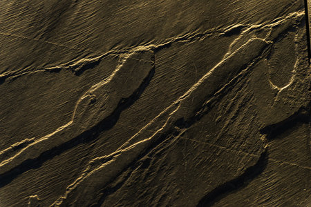 A close up of a rock with a goldish tint. The rock has a rough texture and he is weathered