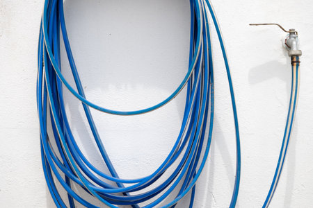 A blue hose is attached to a wall. The hose is connected to a faucet