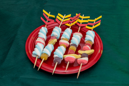 Candy skewers on vibrant red plate with decorative arrows, festive treat table.の写真素材