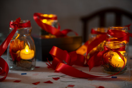Candlelight in glass jars with red ribbons, ideal for festive or cozy settingsの写真素材