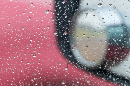 Raindrops on car window, side mirror reflecting a rainy day.