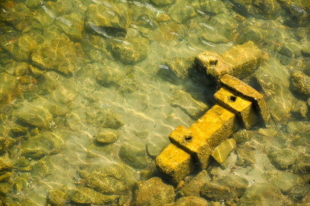 Sunlit underwater rocks and submerged concrete block in clear shallow waterの写真素材