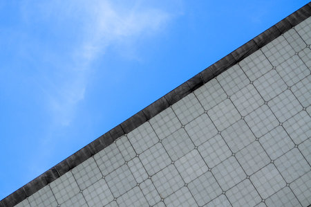 Modern geometric building facade under bright blue sky with wispy clouds.