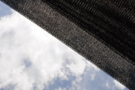 Mesh fabric diagonally draped against bright blue sky with fluffy white clouds