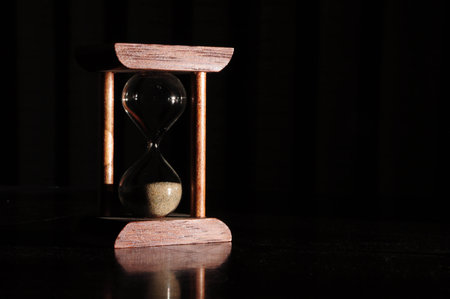 Classic wooden hourglass casting shadows, symbolizing time passage in darkness