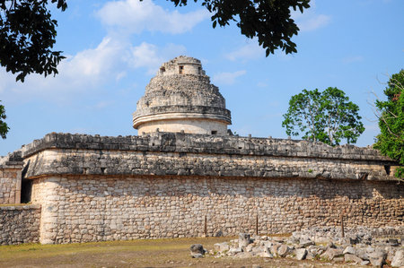 Mayan observatory at Chichen Itza with greenery and clear blue skyの写真素材