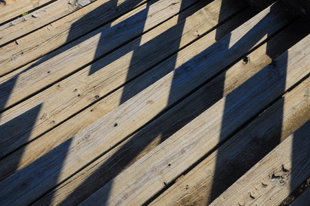 Diagonal shadows on rustic wood planks form a striking geometric patternの写真素材