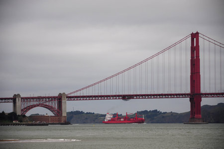 Golden Gate Bridge with red ship passing underneath on a cloudy dayの写真素材