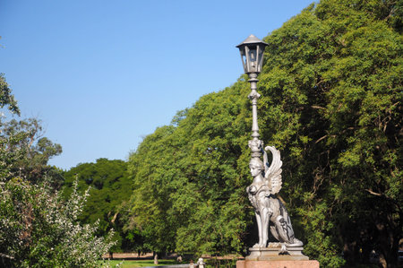 Winged statue holding vintage lamp in green park under blue skyの写真素材